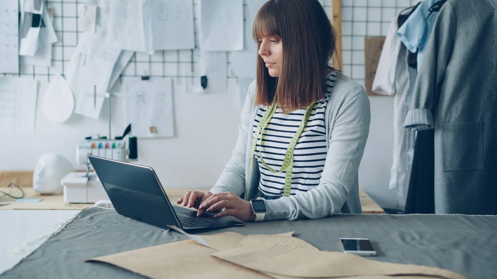 A person working at a laptop in a small studio, surrounded by packaging materials and stock ready to dispatch.