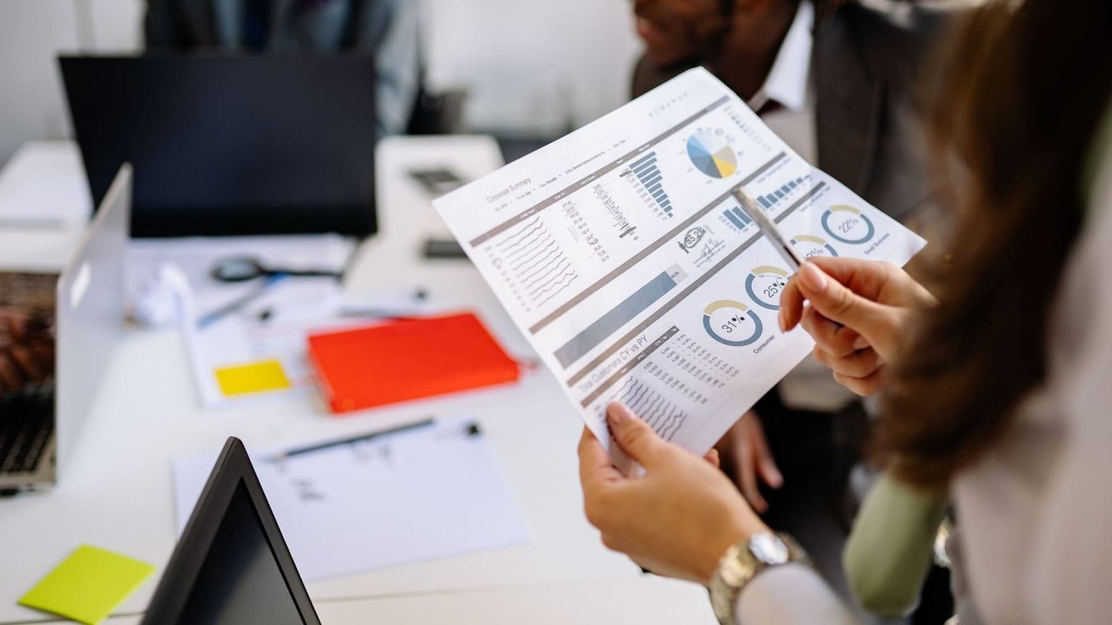 Two people reviewing a printed report of charts and tables together across a desk.