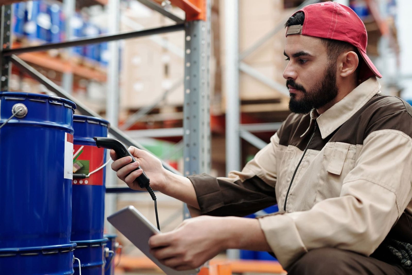 A warehouse worker scanning a drum with a barcode reader, a tablet in his other hand.