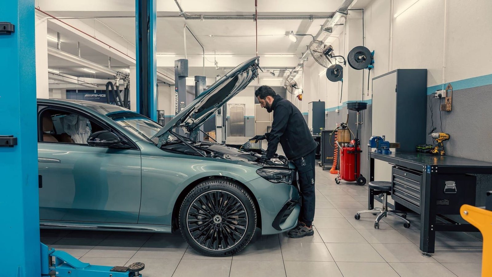 A car raised on a two-post lift in a workshop bay while a technician works at the open engine bay.
