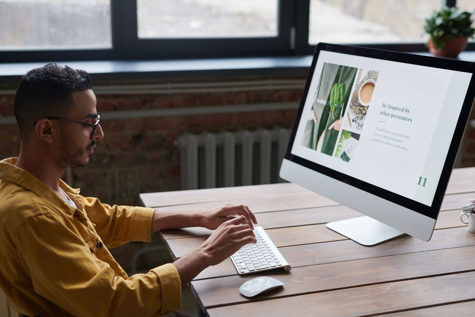A designer working at a desktop computer with a website page layout open on the screen.